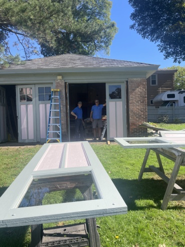 Dan Ruddy and facilities maintenance volunteers pose in the doorway of the museum's on-property garage, with refurbished doors for it in the foreground and being installed.