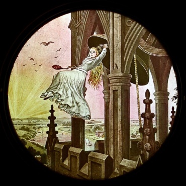 An image of a magic lantern slide from the late 19th century. The circlular image features a young woman suspended between columns with a brightly lite sky and futuristic city landscape behind her.