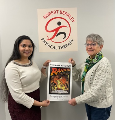 Dr. Singh and Eva Corradino holding a Retro Movie Night Poster in Dr. Singh's office