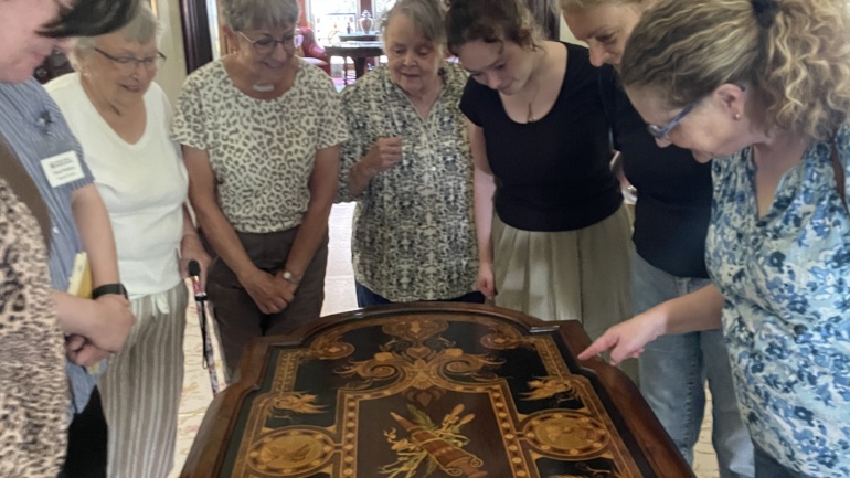 A group of visitors lean in for a closer look at the detail on a table in the parlor of the Richardson-Bates House Museum