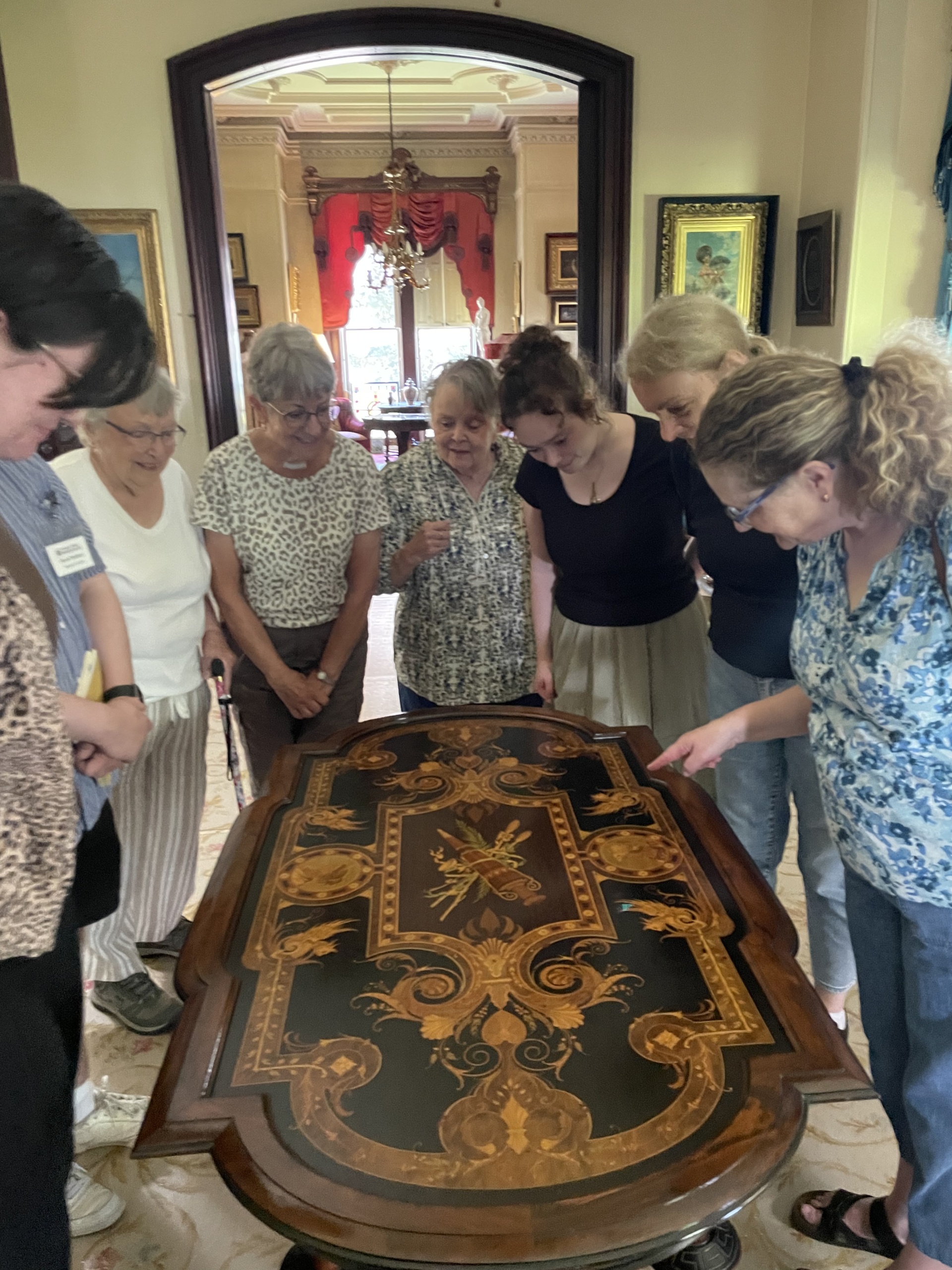 A group of visitors lean in for a closer look at the detail on a table in the parlor of the Richardson-Bates House Museum
