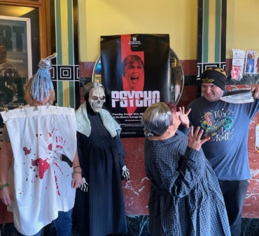 Classic Movie Night volunteers show off their costumes in front of the "Psycho" poster in the lobby of Oswego 7 Cinema.