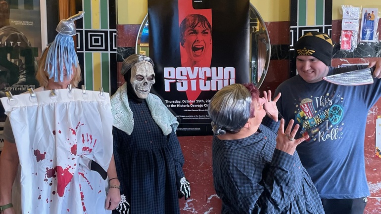 Classic Movie Night volunteers show off their costumes in front of the "Psycho" poster in the lobby of Oswego 7 Cinema.